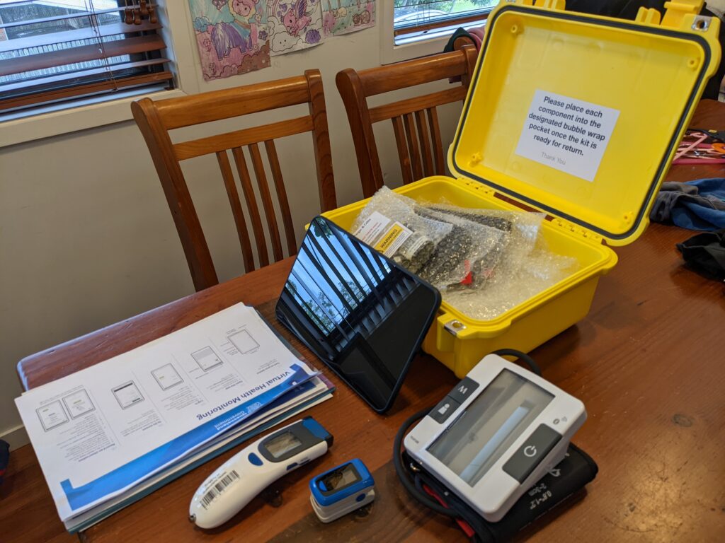 A COVID 'Hospital in the Home' kit from Queensland Health, containing a tablet, thermometer, SpO2 monitor, and blood pressure machine.